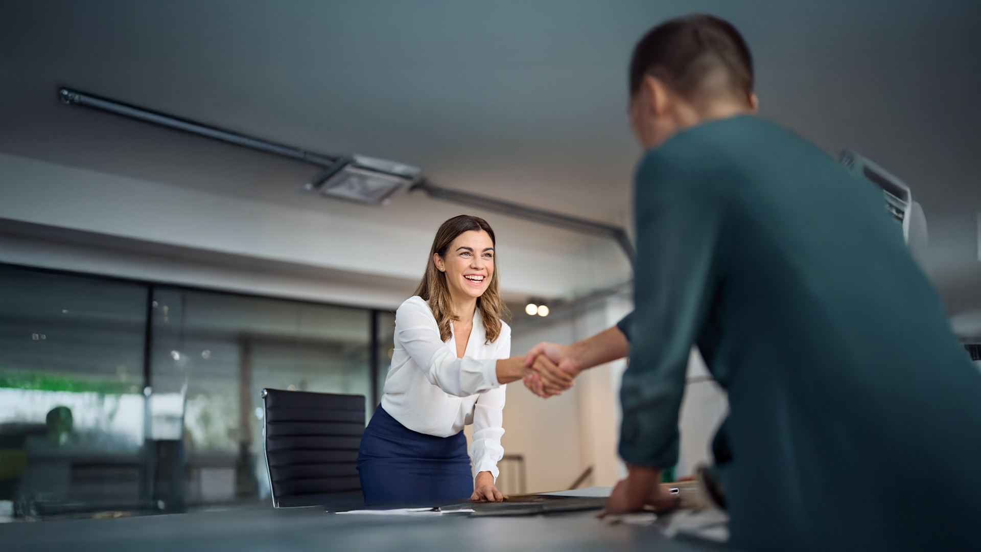 Happy mid aged business woman manager handshaking greeting client in office
